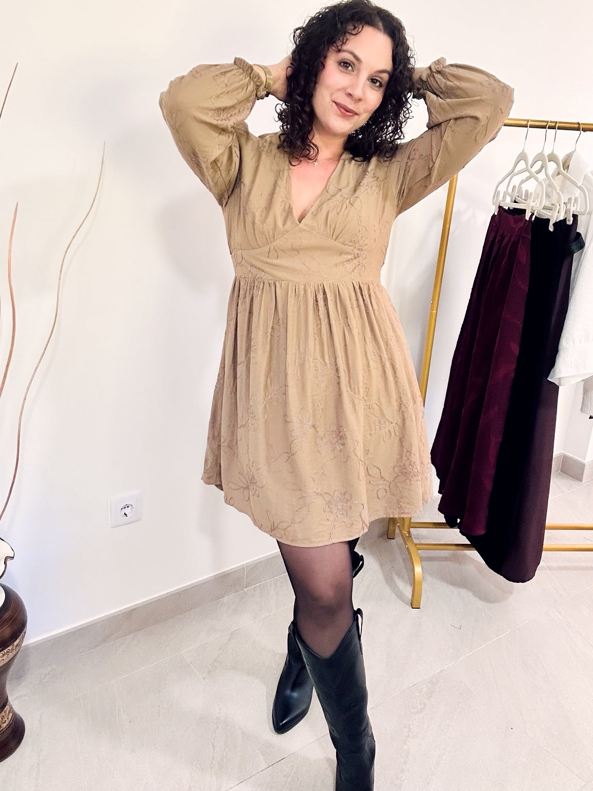 Robe Romy taupe portée en pied, les bras relevés, montrant ses manches longues et sa jupe évasée.