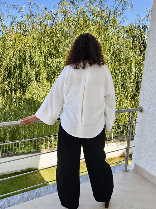 Chemise Melia blanche vue de dos en extérieur, montrant sa coupe ample et son bas arrondi.