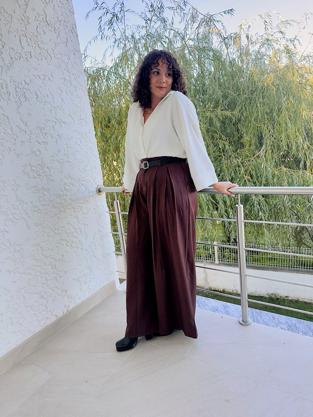 Pantalon Livia marron porté avec une chemise blanche en extérieur, montrant sa longueur et sa coupe ample.