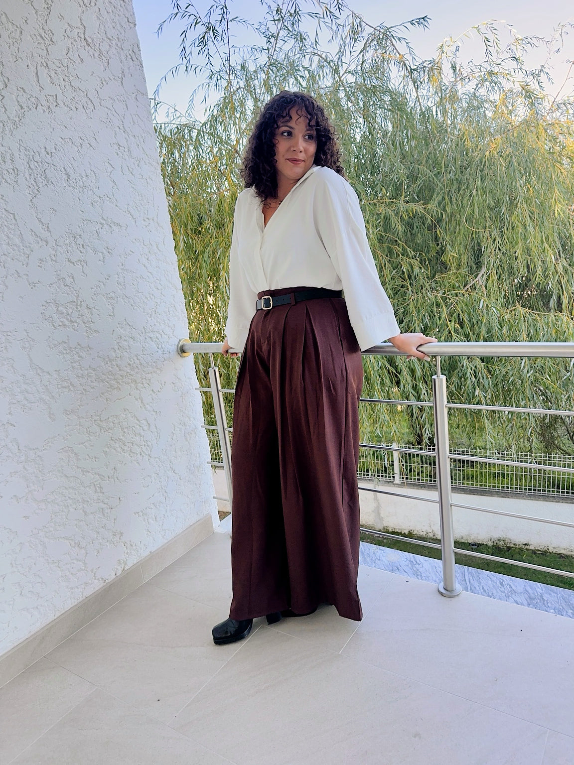 Pantalon Livia marron porté avec une chemise blanche en extérieur, montrant sa longueur et sa coupe ample.