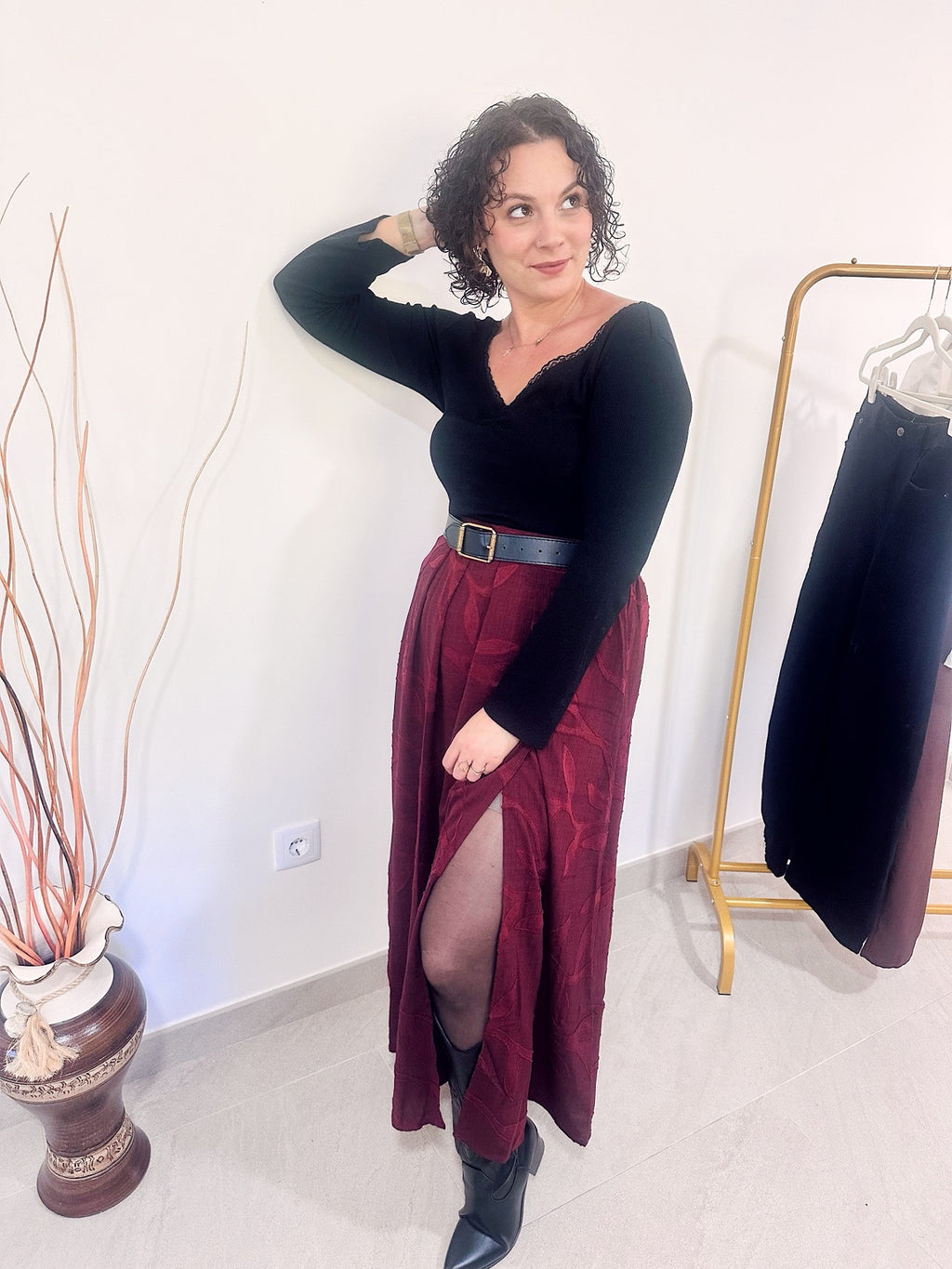 Jupe longue Sienna bordeaux portée avec un haut noir et des bottines, la jambe avancée révélant la fente sur le devant.