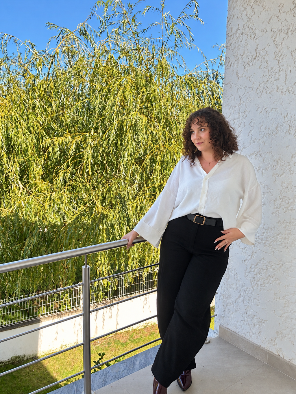 Chemise Melia blanche portée rentrée dans un pantalon noir, silhouette de face en extérieur.