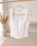 Top corset Eléa blanc à armatures et découpes verticales suspendu sur cintre